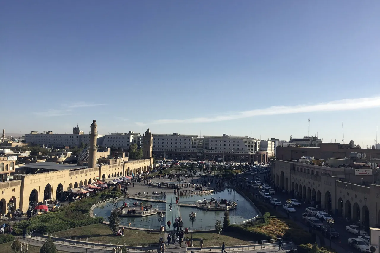 A city square with fountains below a citadel, seen from above