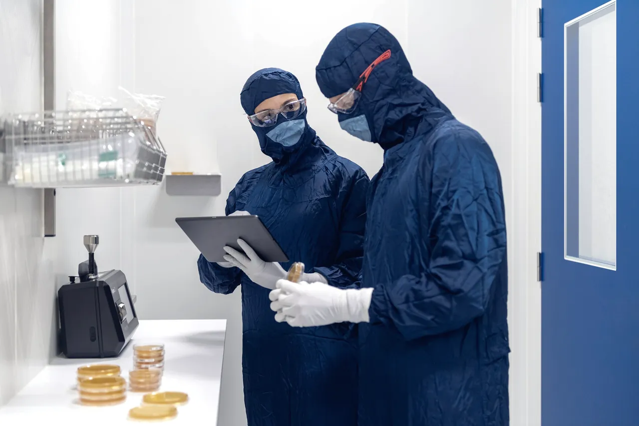 Two people in cleanroom suits reading a tablet