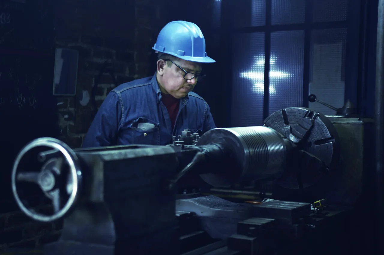 A machinist in a hard hat and safety glasses working at a lathe