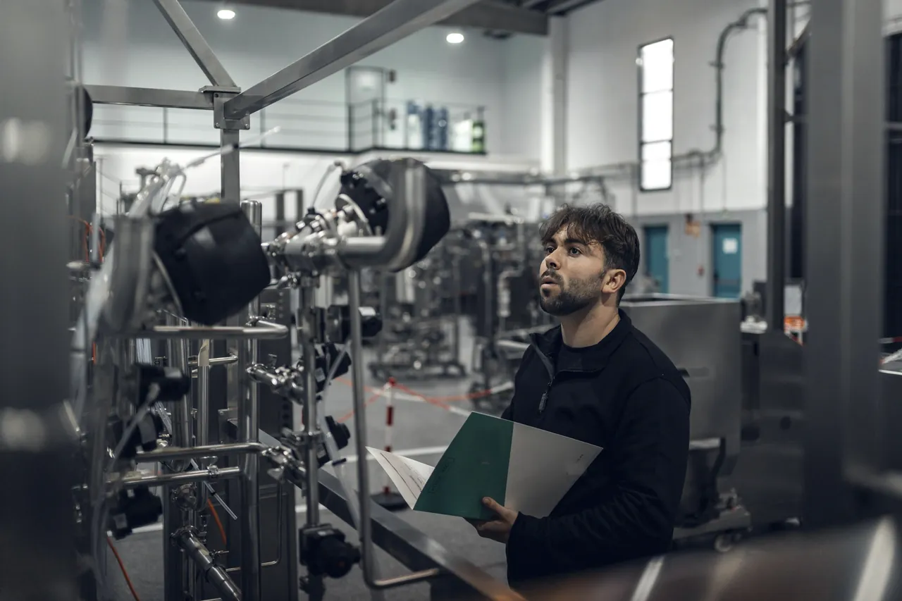 A man holding a folder looks up at process equipment in a plant